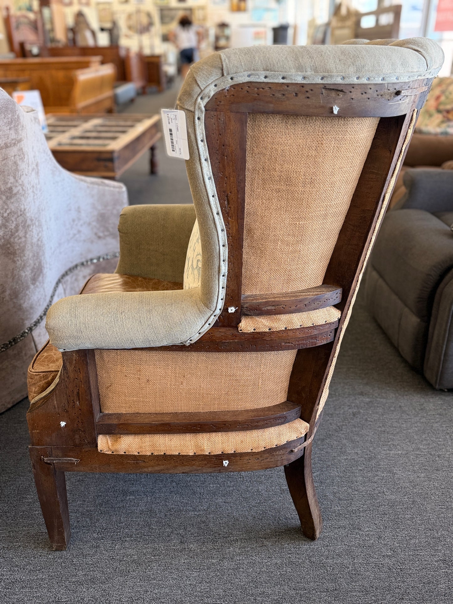 A classic wingback armchair featuring a beige channel-tufted fabric back, distressed brown leather seat cushion, dark wooden legs, and decorative nailhead trim.