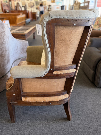 A classic wingback armchair featuring a beige channel-tufted fabric back, distressed brown leather seat cushion, dark wooden legs, and decorative nailhead trim.