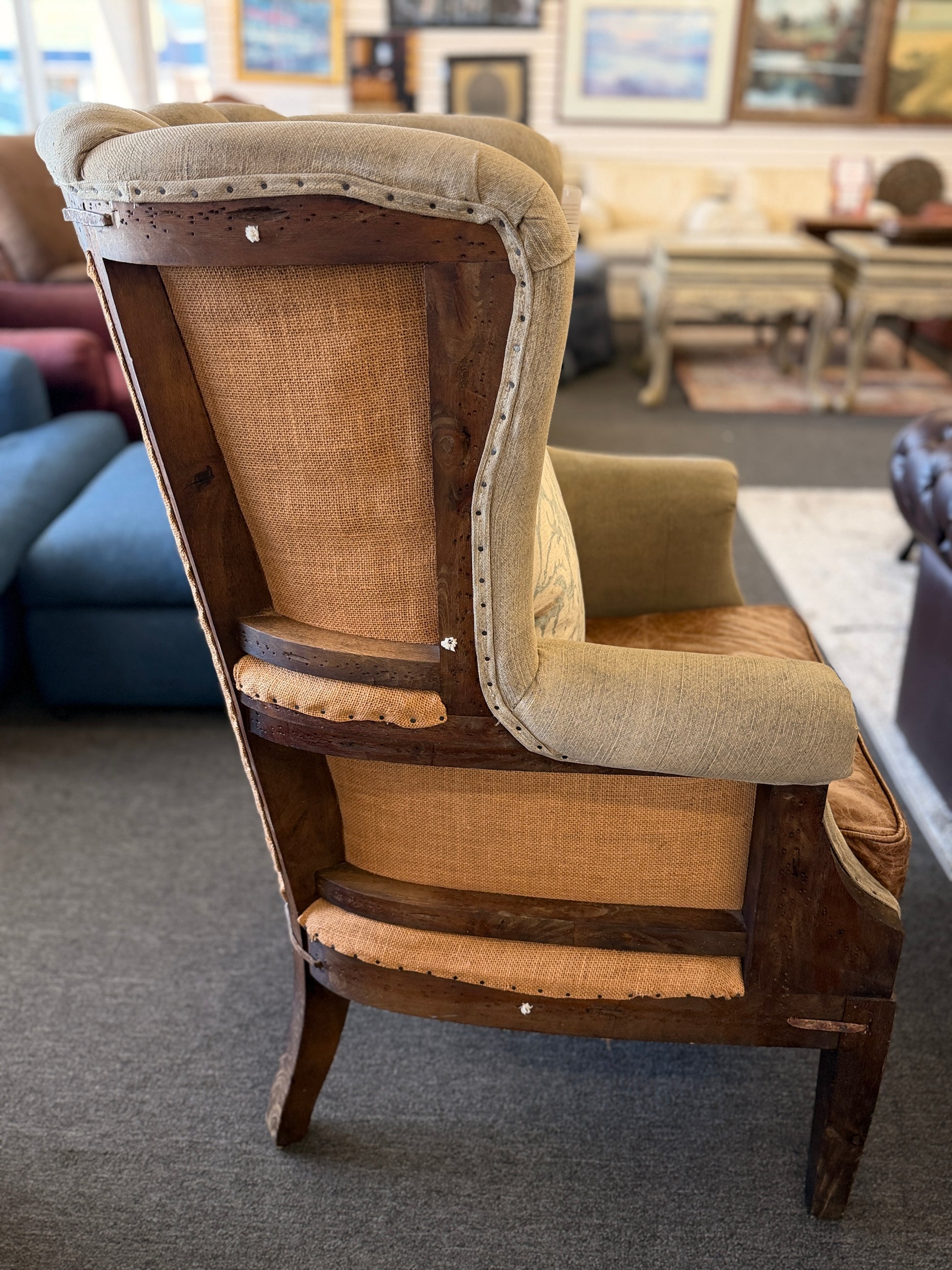 A classic wingback armchair featuring a beige channel-tufted fabric back, distressed brown leather seat cushion, dark wooden legs, and decorative nailhead trim.