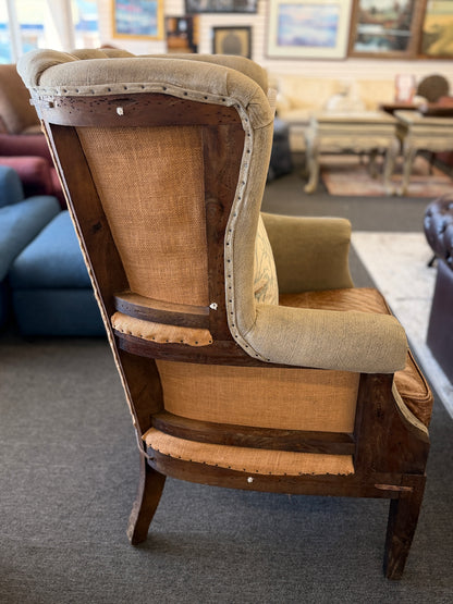 A classic wingback armchair featuring a beige channel-tufted fabric back, distressed brown leather seat cushion, dark wooden legs, and decorative nailhead trim.