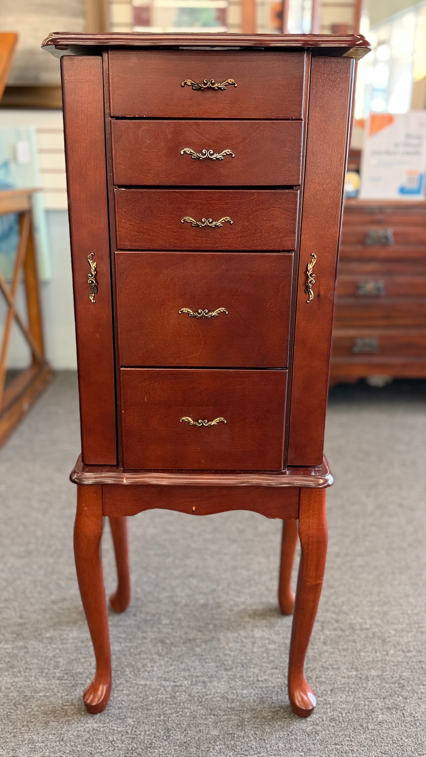 A tall cherry-finished wooden jewelry cabinet on cabriole legs featuring pull-out drawers, swinging side doors, and a flip-top vanity mirror.