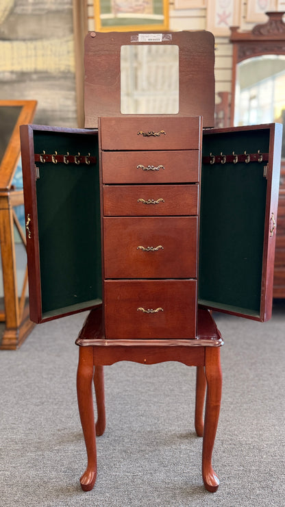 A tall cherry-finished wooden jewelry cabinet on cabriole legs featuring pull-out drawers, swinging side doors, and a flip-top vanity mirror.
