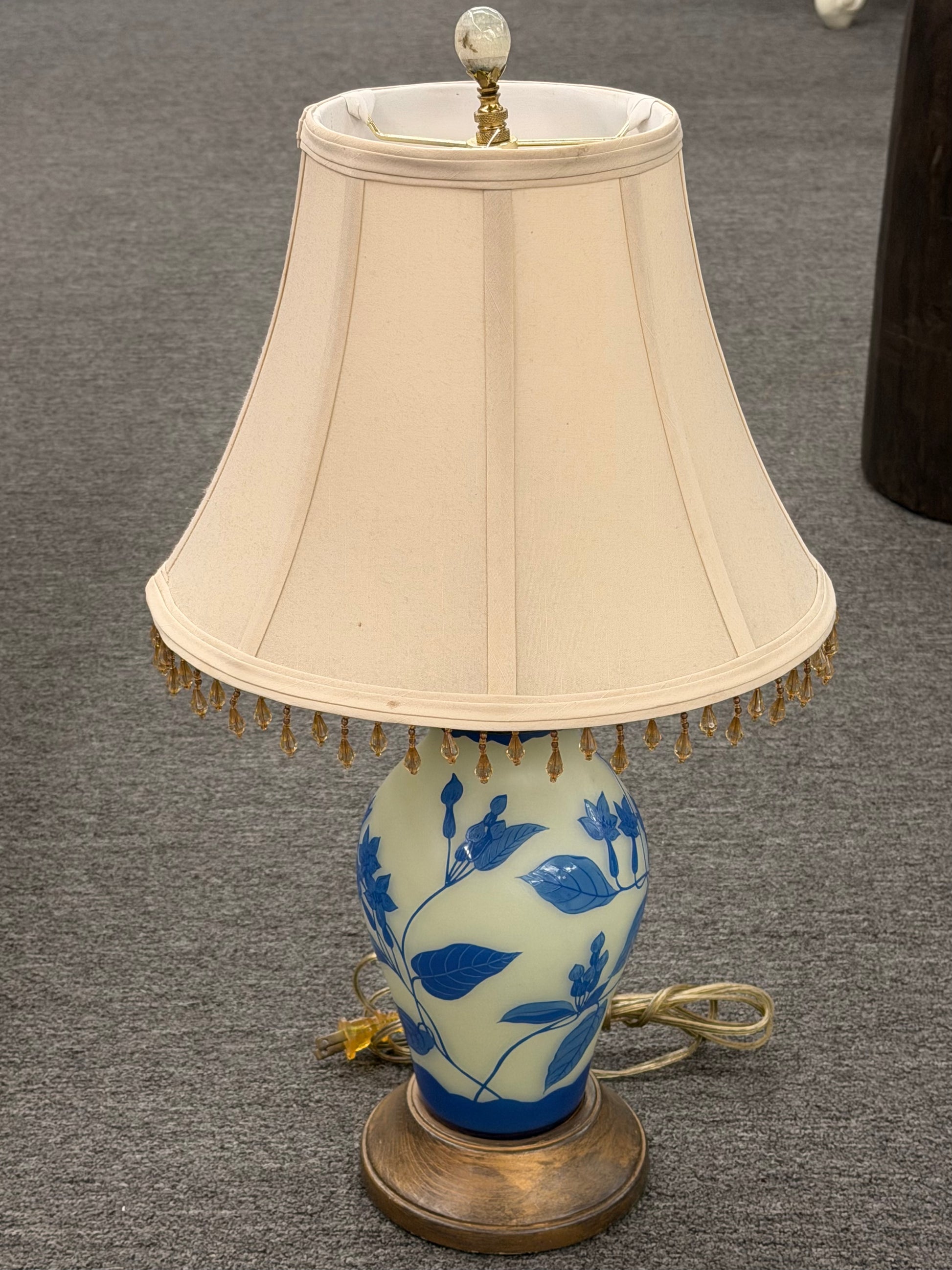 Traditional Chinoiserie blue and cream floral table lamp featuring a ceramic base with a blue floral design and a beige lampshade with beaded fringe decorative trim at 2nd Debut Houston consignment showroom