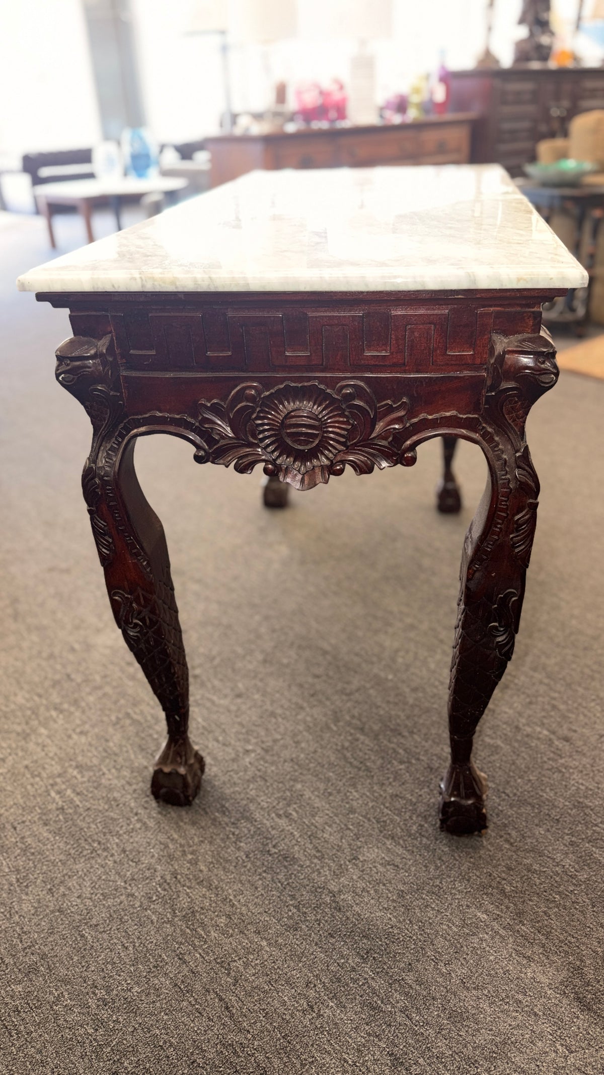 A Chippendale-style marble-top console table featuring an intricately carved mahogany apron, Greek key border, and cabriole legs with ball-and-claw feet in good condition.