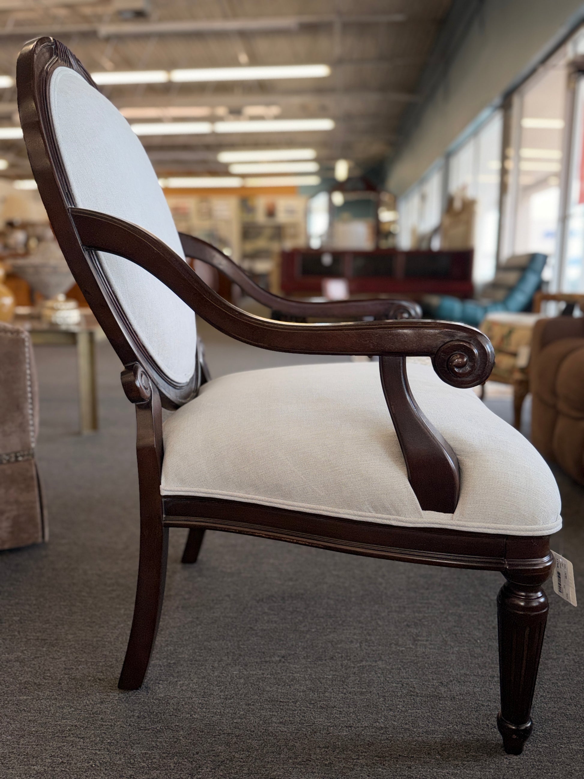 Classic oval-back accent chair with a dark wood frame, light beige upholstered seat and back, padded armrests, and fluted tapered wooden legs.