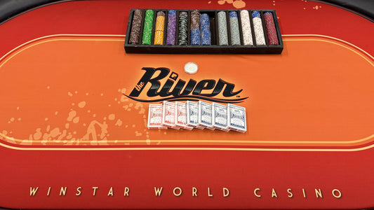 An oval-shaped Texas Hold'em poker table featuring a bright orange and red branded felt surface, black padded armrest ring, wood base, poker chips, and playing cards.