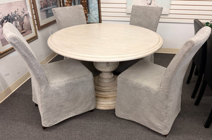 A coastal-farmhouse dining set featuring a round whitewashed pedestal table and four light gray skirted slipcover chairs in good condition.