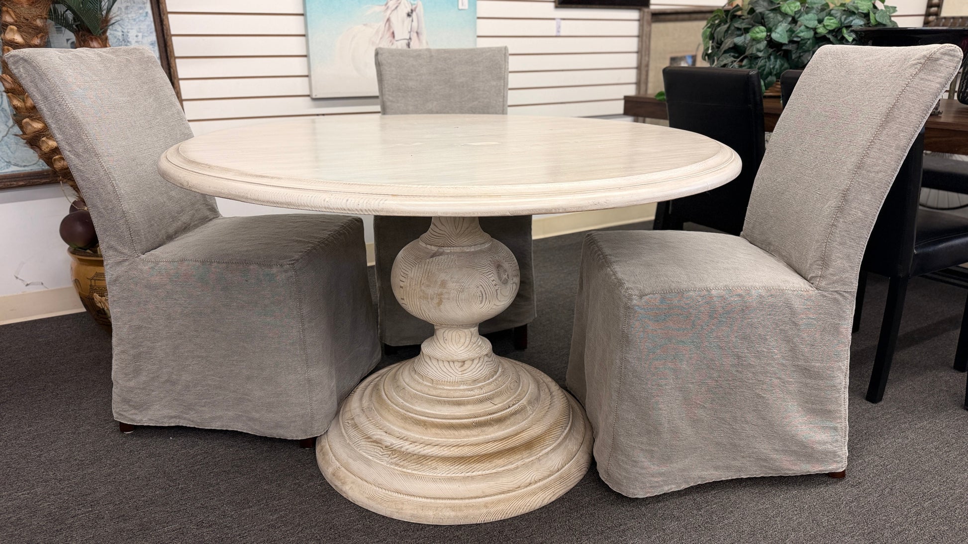 A coastal-farmhouse dining set featuring a round whitewashed pedestal table and four light gray skirted slipcover chairs in good condition.