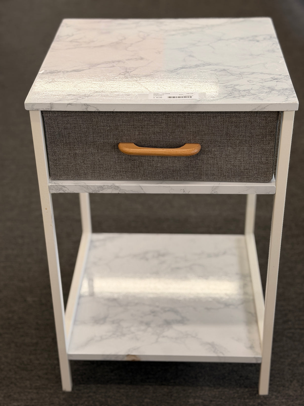 A compact nightstand featuring a white metal frame, faux marble top and bottom shelves, and a gray fabric drawer with a wooden handle in good condition.