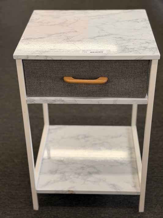 A compact nightstand featuring a white metal frame, faux marble top and bottom shelves, and a gray fabric drawer with a wooden handle in good condition.