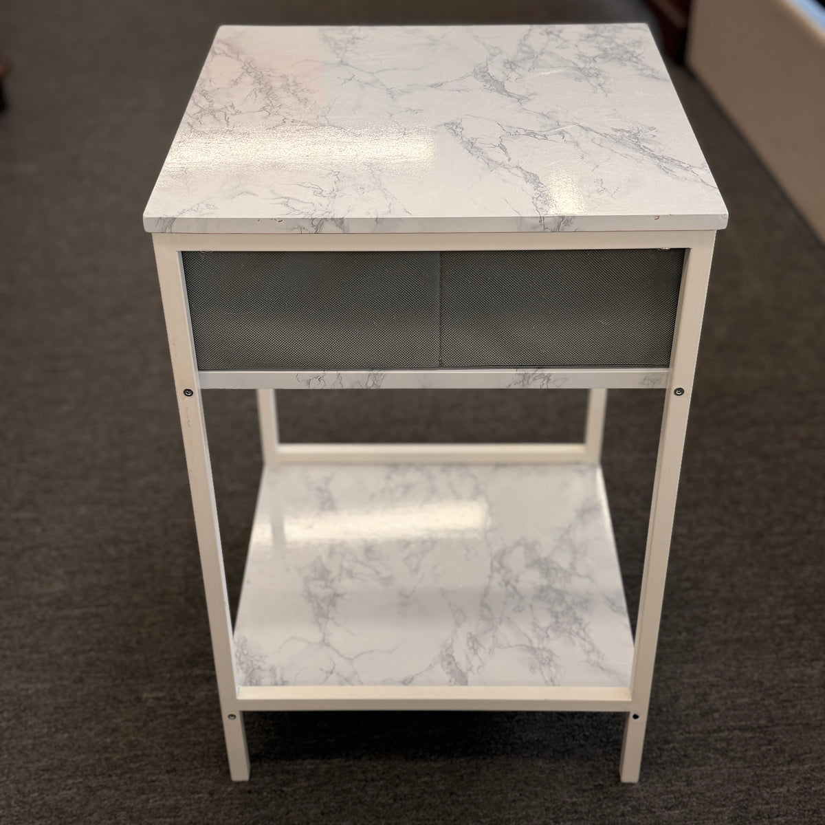 A compact nightstand featuring a white metal frame, faux marble top and bottom shelves, and a gray fabric drawer with a wooden handle in good condition.