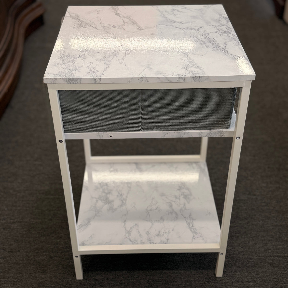 A compact nightstand featuring a white metal frame, faux marble top and bottom shelves, and a gray fabric drawer with a wooden handle in good condition.