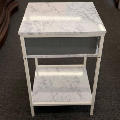 A compact nightstand featuring a white metal frame, faux marble top and bottom shelves, and a gray fabric drawer with a wooden handle in good condition.