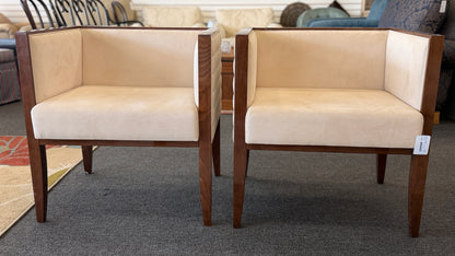 A pair of contemporary squared-off accent chairs with light beige suede-like upholstery, an exposed dark wood outer frame, and subtle quilted tufting on the side panels.