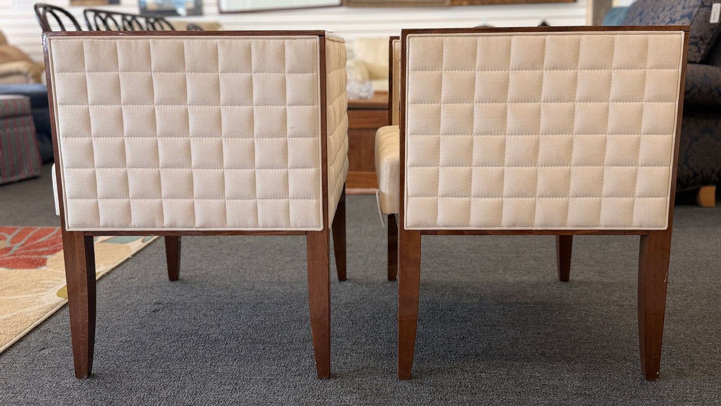 A pair of contemporary squared-off accent chairs with light beige suede-like upholstery, an exposed dark wood outer frame, and subtle quilted tufting on the side panels.