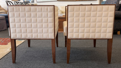 A pair of contemporary squared-off accent chairs with light beige suede-like upholstery, an exposed dark wood outer frame, and subtle quilted tufting on the side panels.