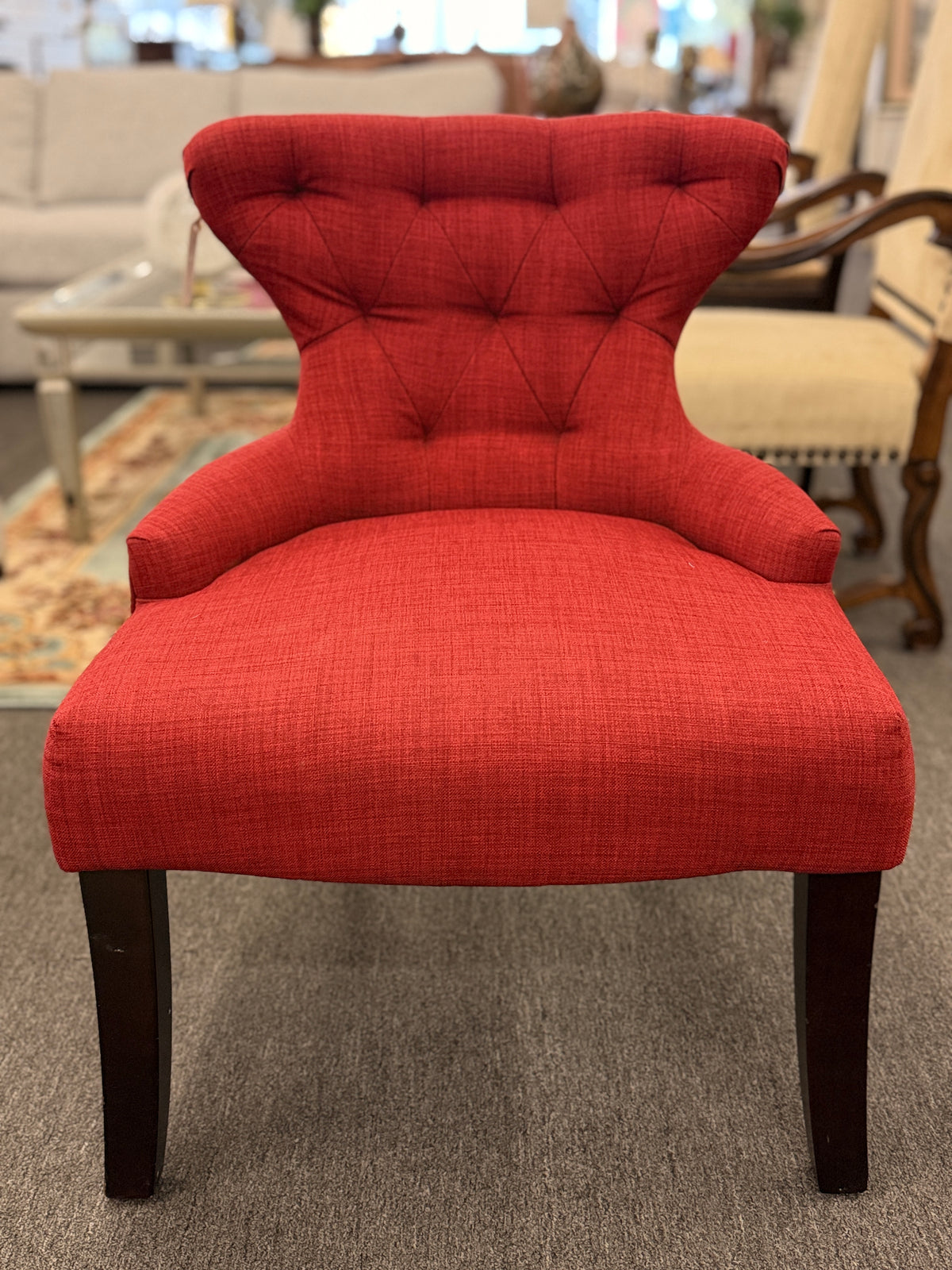 A contemporary accent armchair upholstered in textured burnt-orange fabric with button-tufted back detailing and dark-finished tapered legs in good condition.