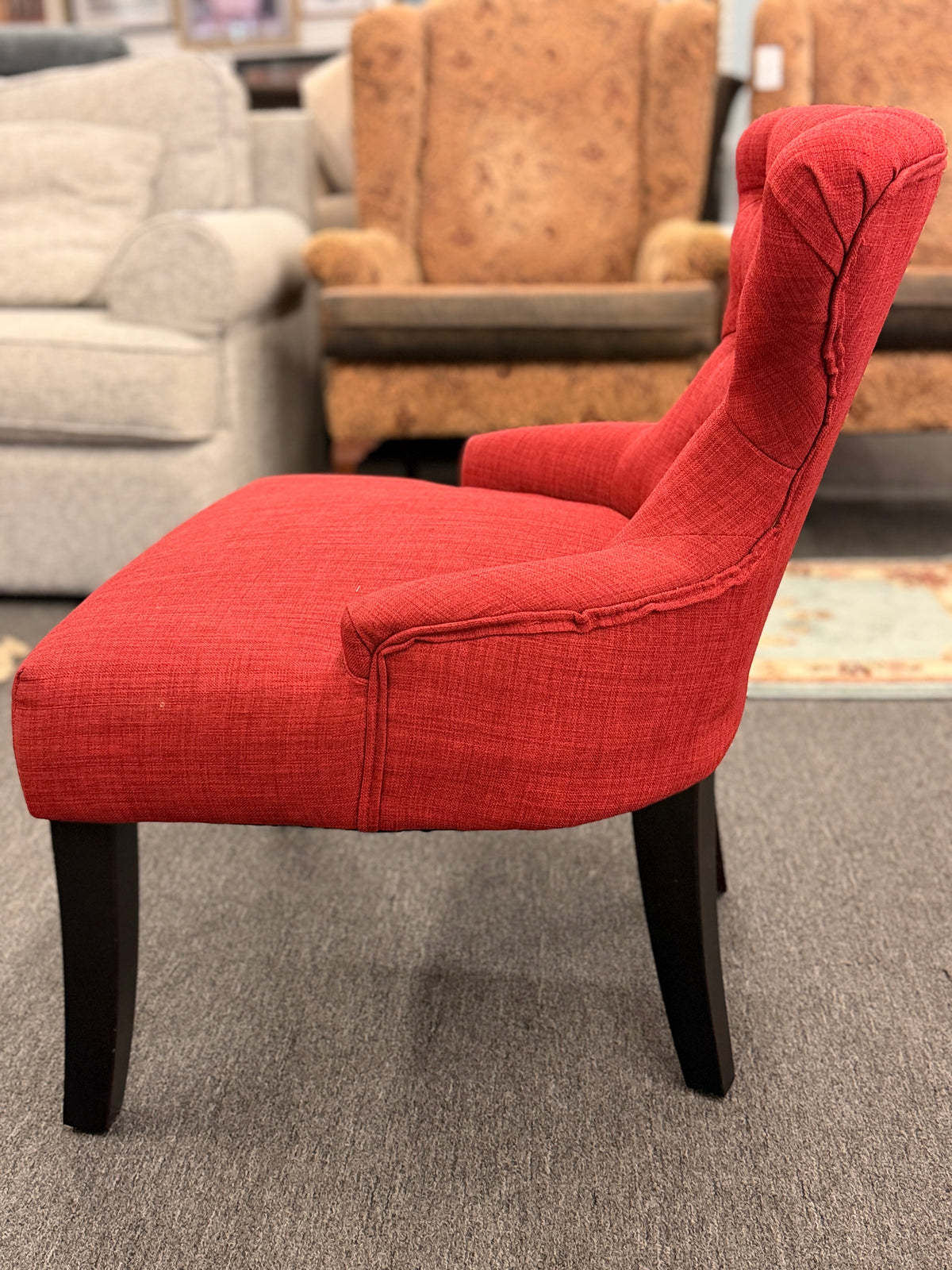 A contemporary accent armchair upholstered in textured burnt-orange fabric with button-tufted back detailing and dark-finished tapered legs in good condition.
