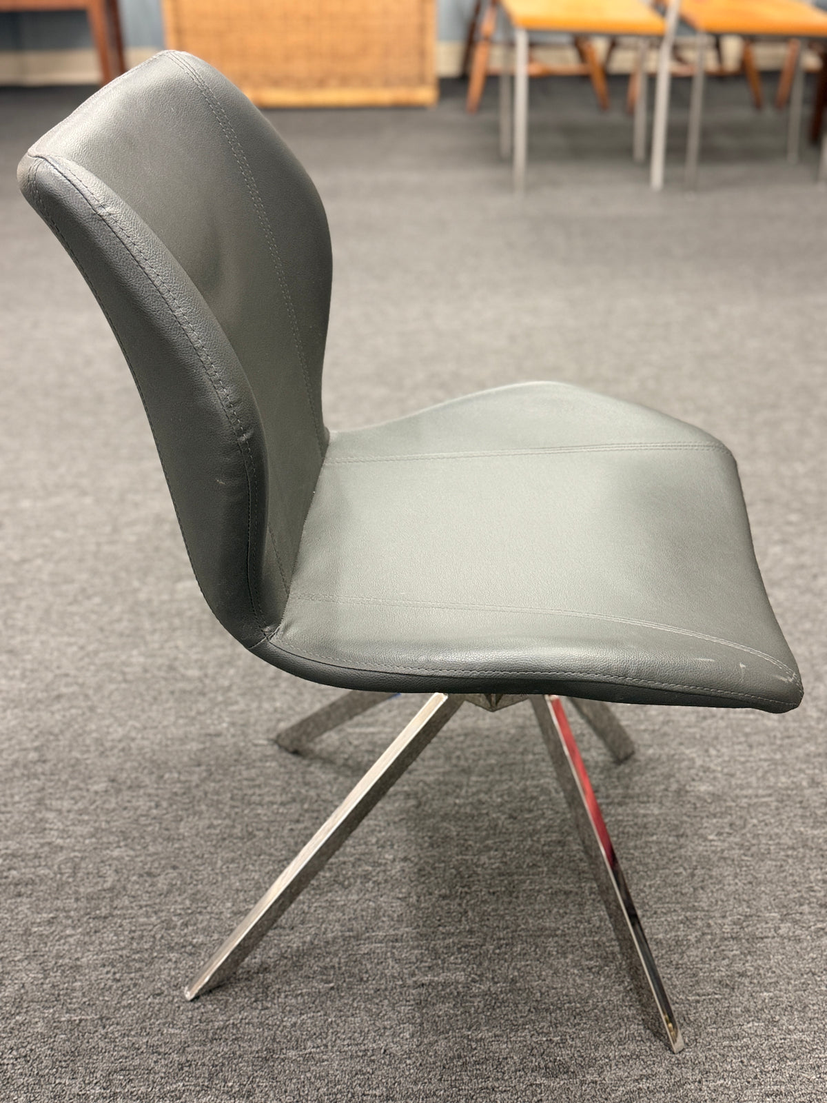 An accent office chair featuring sleek charcoal-gray faux leather upholstery with stitched seams, set on four angled chrome legs in good condition.