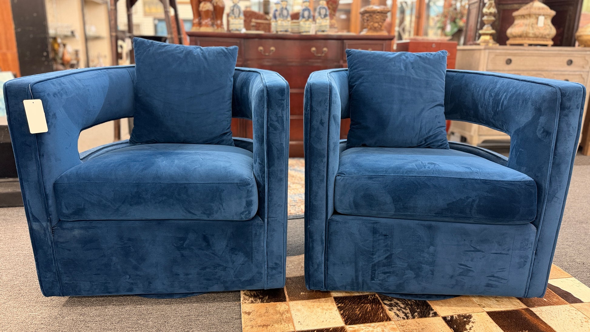 A pair of contemporary curved barrel-back swivel armchairs featuring open cutout backrests and matching square toss pillows.