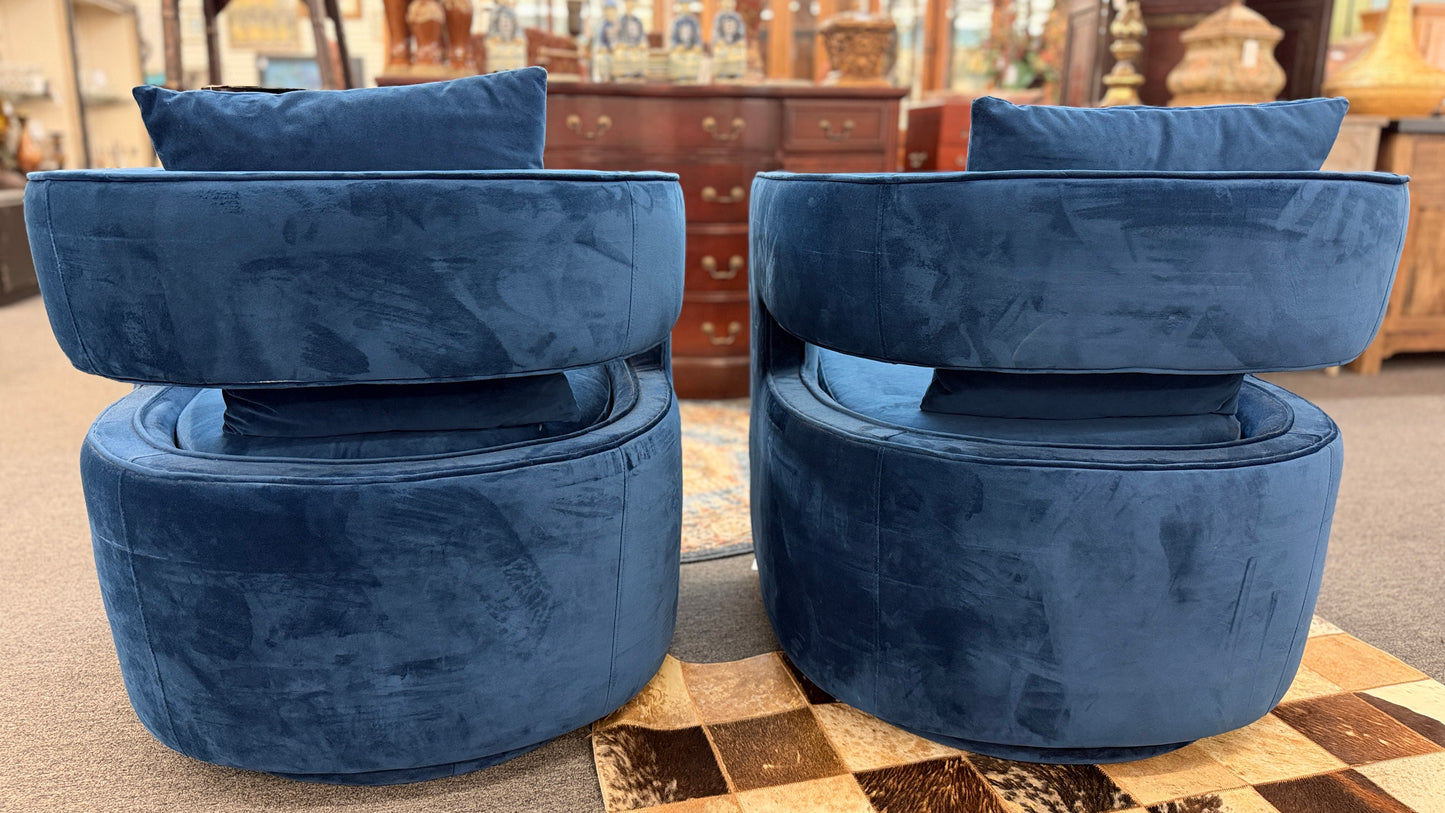 A pair of contemporary curved barrel-back swivel armchairs featuring open cutout backrests and matching square toss pillows.