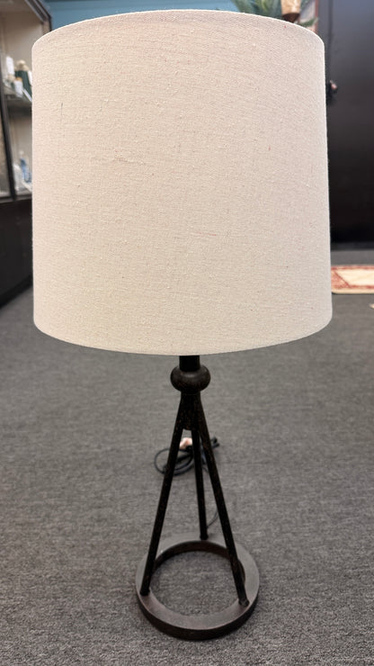 A contemporary minimalist table lamp with a dark bronze or black tripod metal base on a ring stand, topped with an oversized cylindrical off-white linen drum shade in good condition.