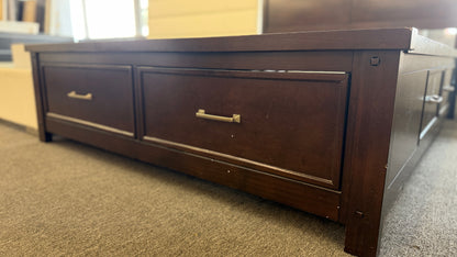 A contemporary dark-finished queen bed frame featuring a simple paneled headboard, wooden slat support, and two built-in storage drawers in the footboard.