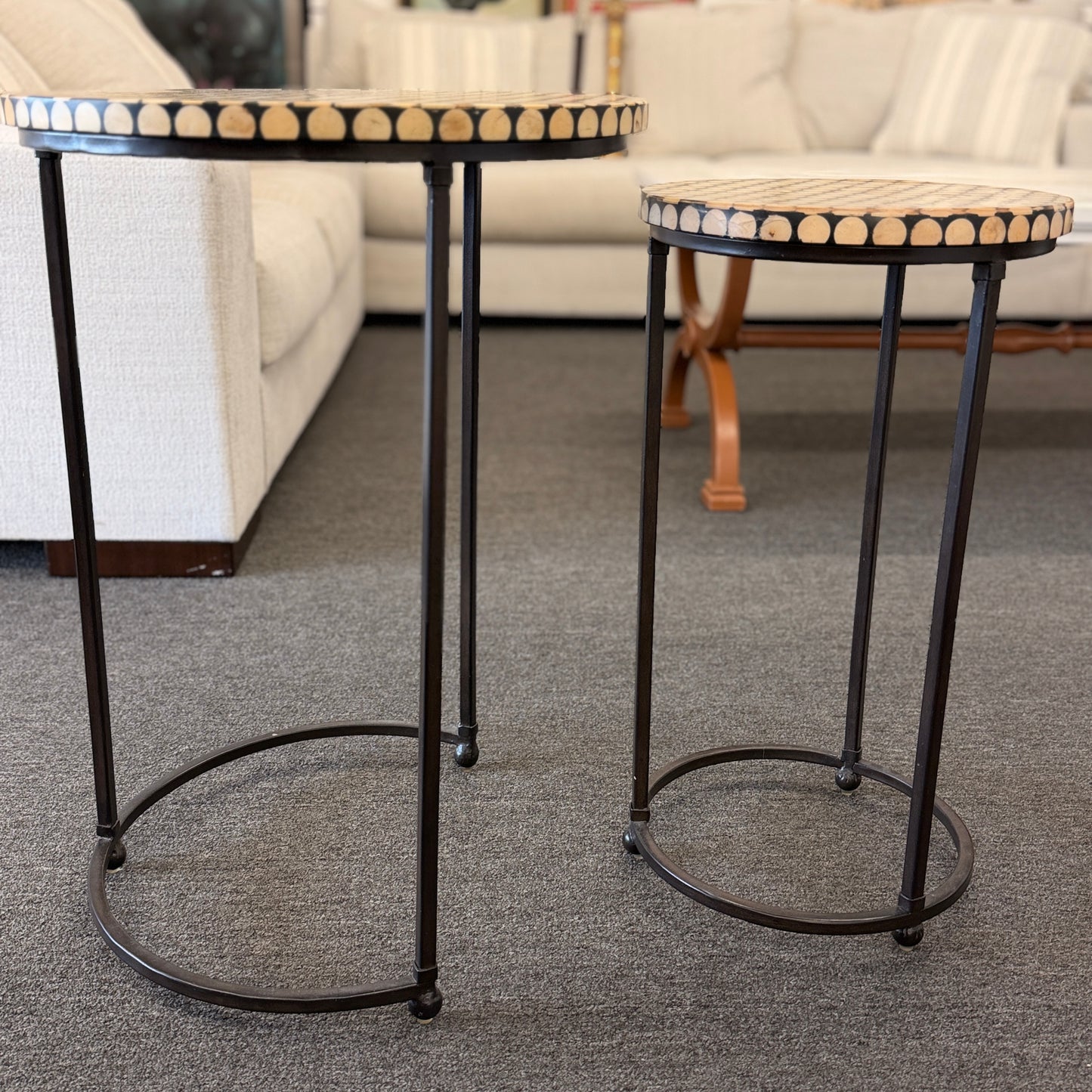 A two-piece contemporary nesting side table set featuring patterned mosaic wooden tops on slim iron tripod frames.