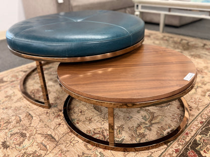 A two-piece contemporary nesting coffee table set featuring a petrol blue tufted leather round ottoman and a lower round walnut wood table on metal sled bases in good condition.