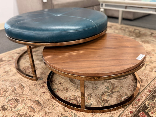 A two-piece contemporary nesting coffee table set featuring a petrol blue tufted leather round ottoman and a lower round walnut wood table on metal sled bases in good condition.