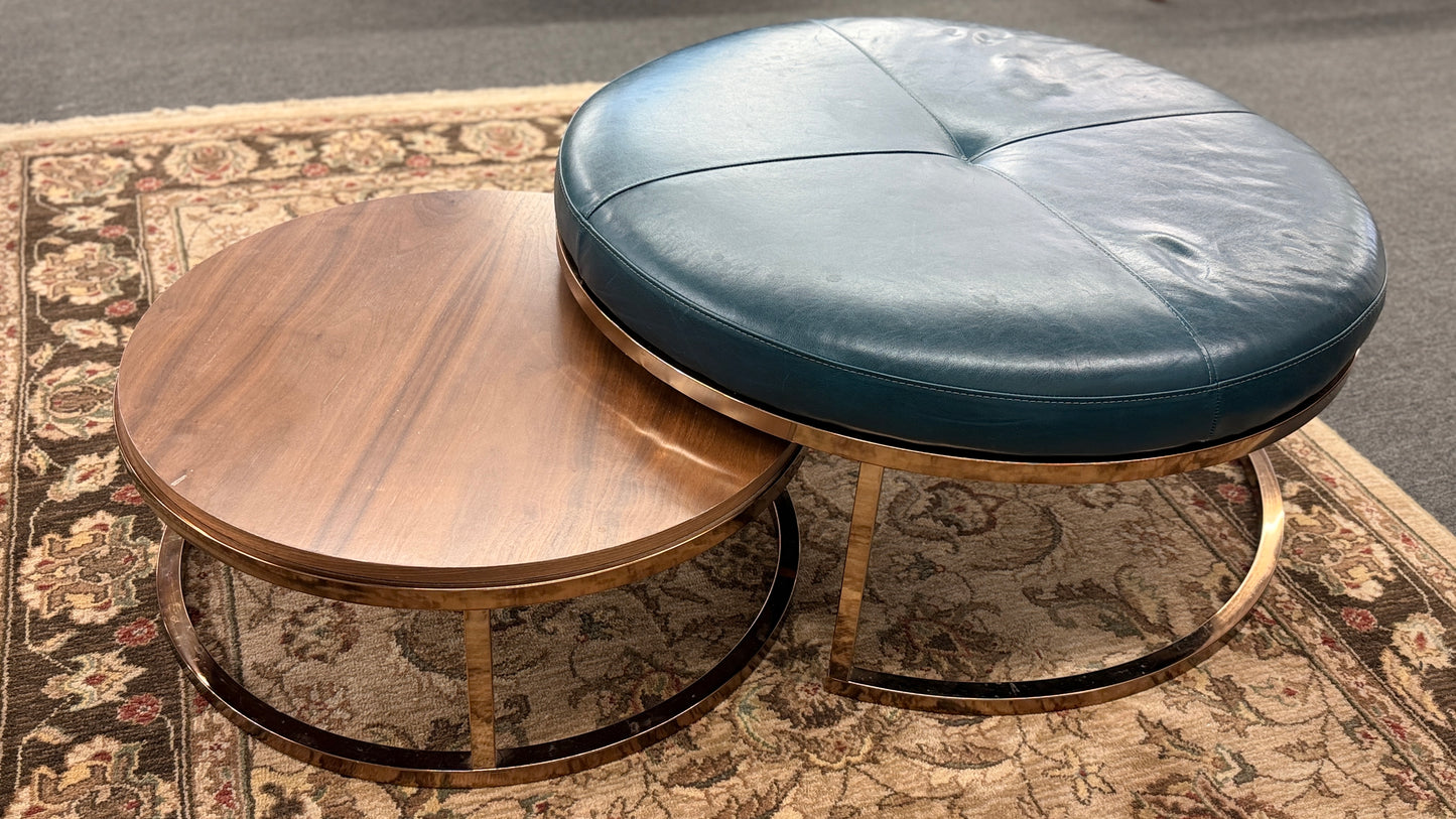 A two-piece contemporary nesting coffee table set featuring a petrol blue tufted leather round ottoman and a lower round walnut wood table on metal sled bases in good condition.