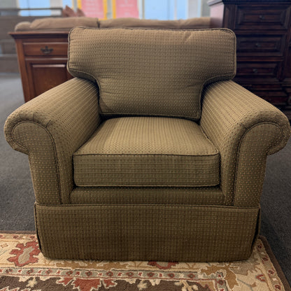 A cozy oversized swivel armchair with textured olive-green patterned fabric, rolled arms, a T-cushion backrest, and a full fabric skirt base in good condition.