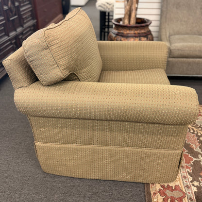 A cozy oversized swivel armchair with textured olive-green patterned fabric, rolled arms, a T-cushion backrest, and a full fabric skirt base in good condition.