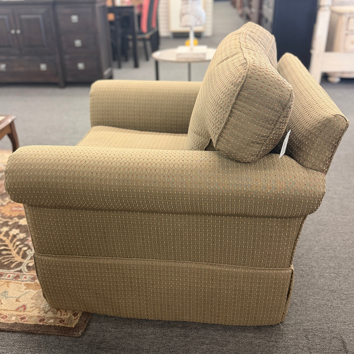A cozy oversized swivel armchair with textured olive-green patterned fabric, rolled arms, a T-cushion backrest, and a full fabric skirt base in good condition.