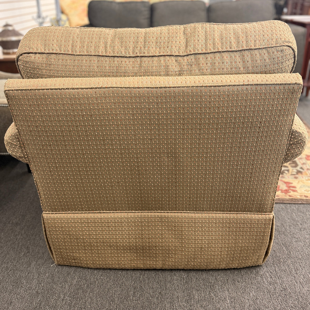 A cozy oversized swivel armchair with textured olive-green patterned fabric, rolled arms, a T-cushion backrest, and a full fabric skirt base in good condition.