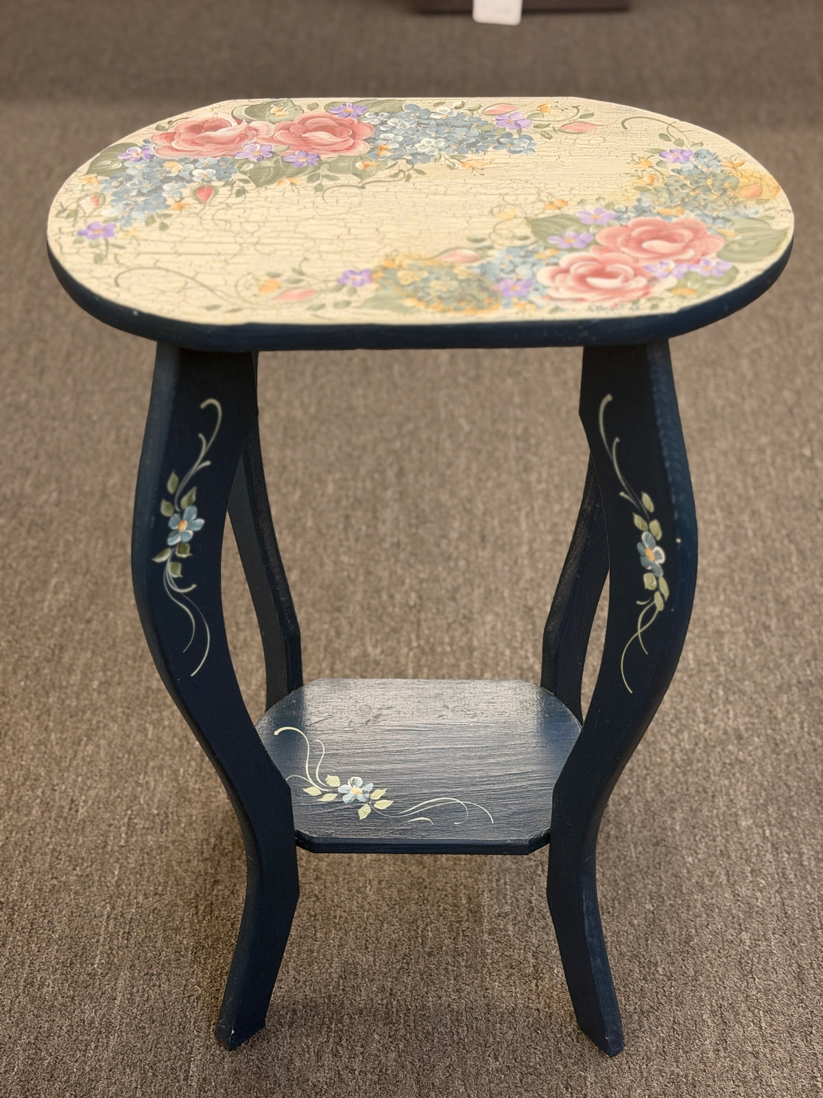 A dark blue accent table decorated with painted floral motifs on both the top surface and the lower shelf in good condition.