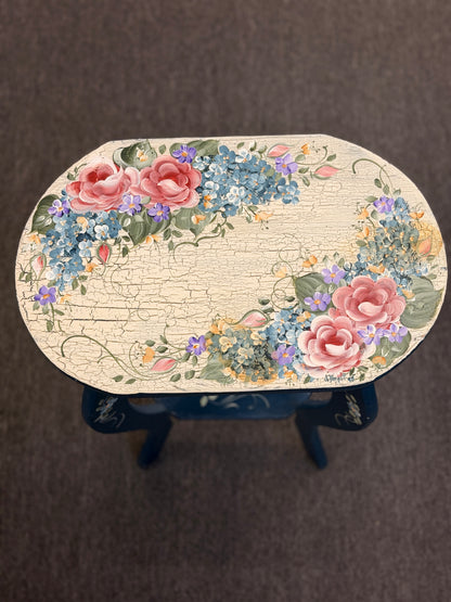 A dark blue accent table decorated with painted floral motifs on both the top surface and the lower shelf in good condition.