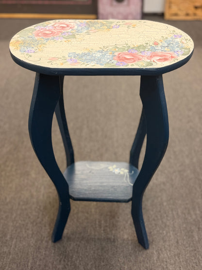 A dark blue accent table decorated with painted floral motifs on both the top surface and the lower shelf in good condition.