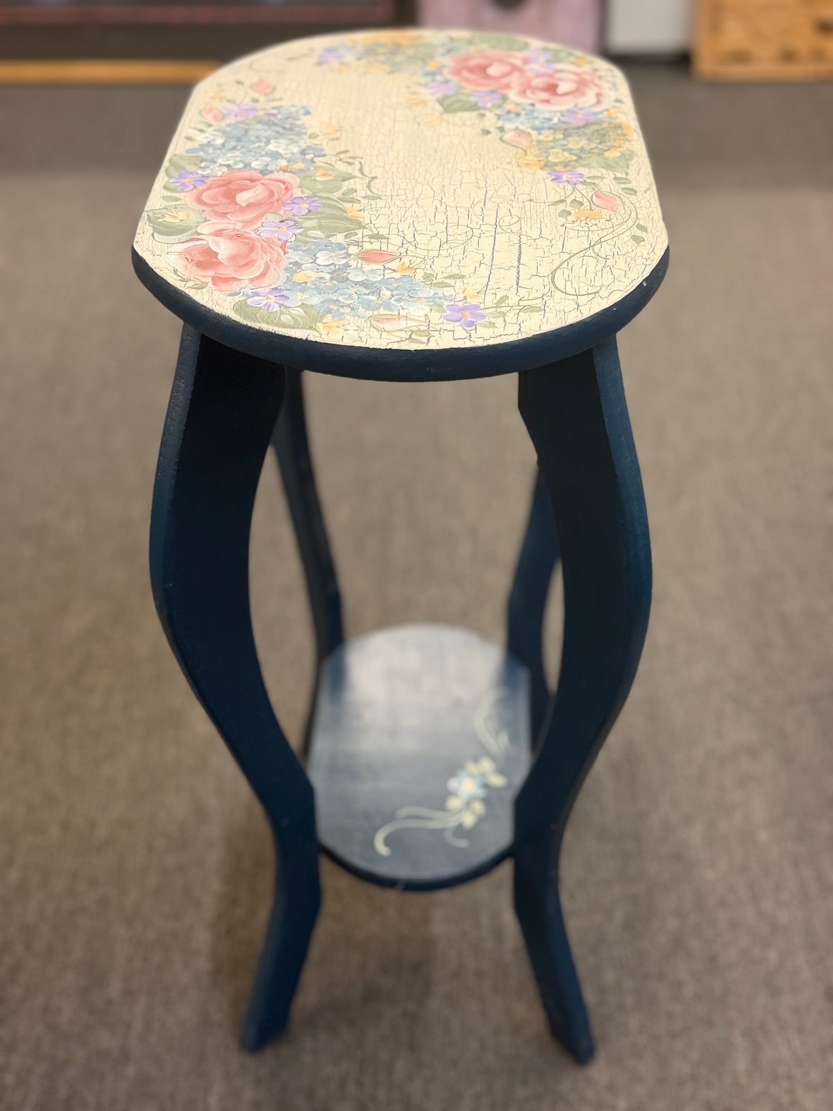 A dark blue accent table decorated with painted floral motifs on both the top surface and the lower shelf in good condition.