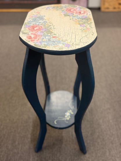 A dark blue accent table decorated with painted floral motifs on both the top surface and the lower shelf in good condition.
