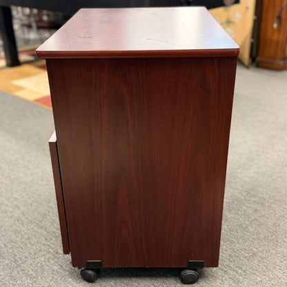 A compact mobile storage cabinet in a dark cherry finish featuring an open top shelf, double cabinet doors with curved black handles, and rolling wheels.