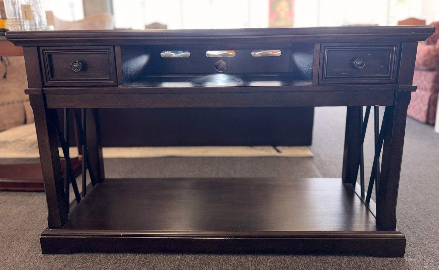 A dark-finished media console TV stand featuring X-brace side details, two small top drawers, a central open cubby with cable holes, and a large bottom shelf.