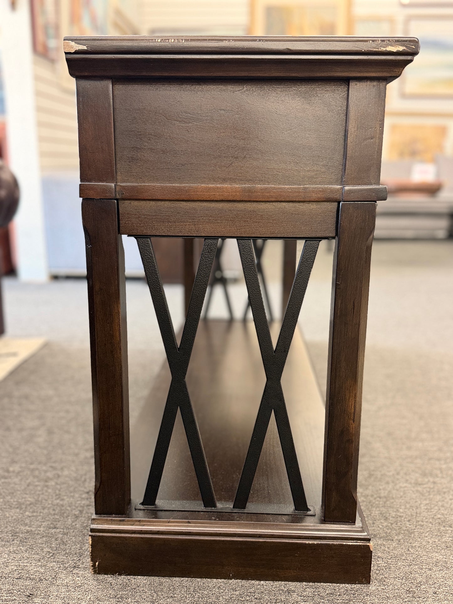 A dark-finished media console TV stand featuring X-brace side details, two small top drawers, a central open cubby with cable holes, and a large bottom shelf.