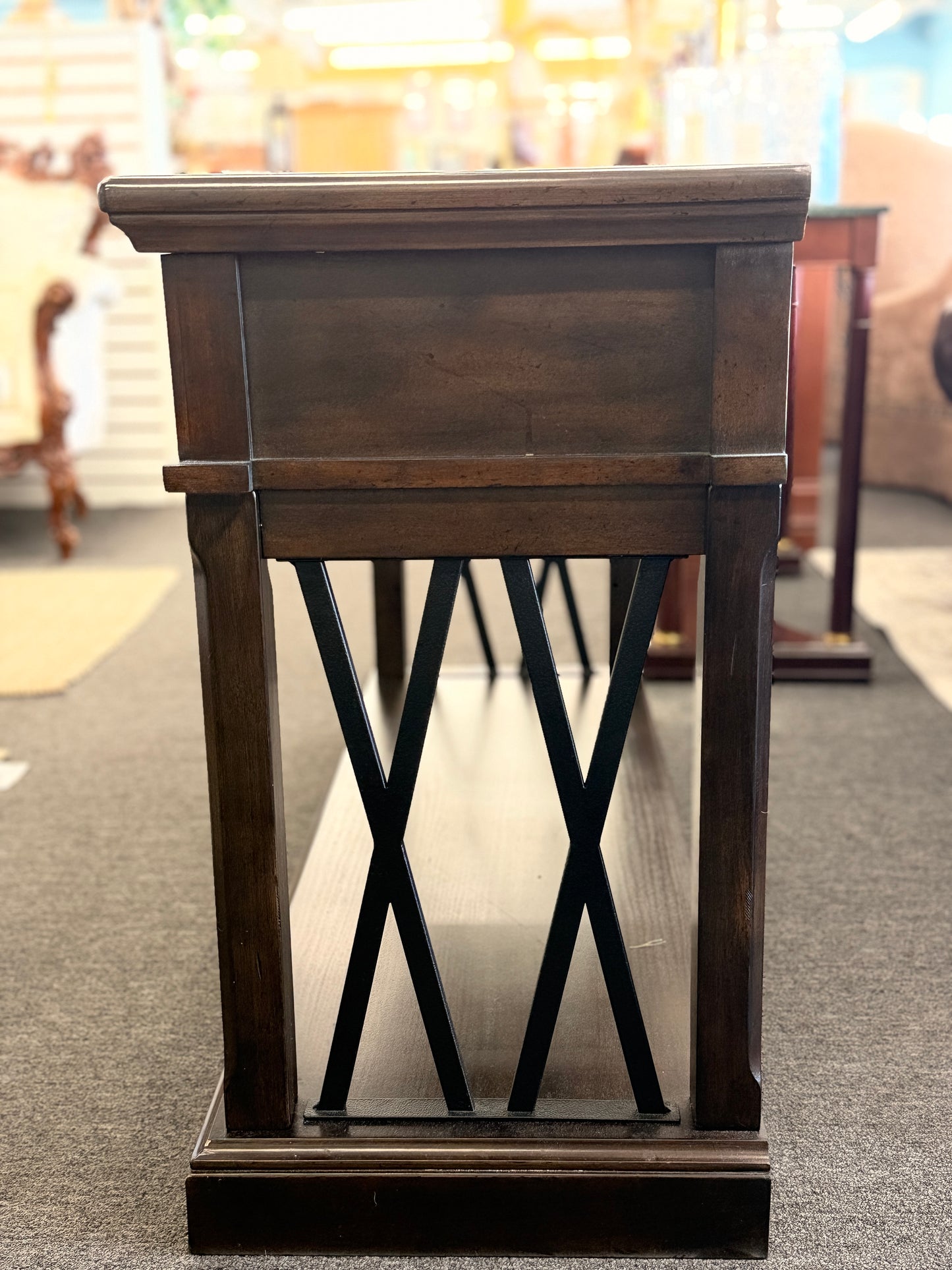 A dark-finished media console TV stand featuring X-brace side details, two small top drawers, a central open cubby with cable holes, and a large bottom shelf.