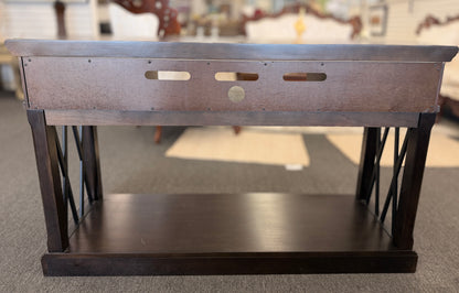 A dark-finished media console TV stand featuring X-brace side details, two small top drawers, a central open cubby with cable holes, and a large bottom shelf.