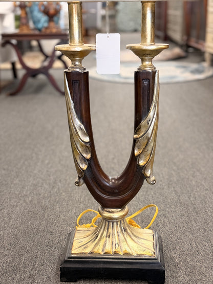 Decorative table lamp featuring a dark U-shaped body with metallic leaf accents, a fluted metallic pedestal, black square base, and a large cream-colored drum shade.