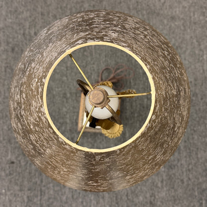 A decorative table lamp featuring a slender white floral ceramic body, a metallic-finish shade, brass accents, and a gold tassel.
