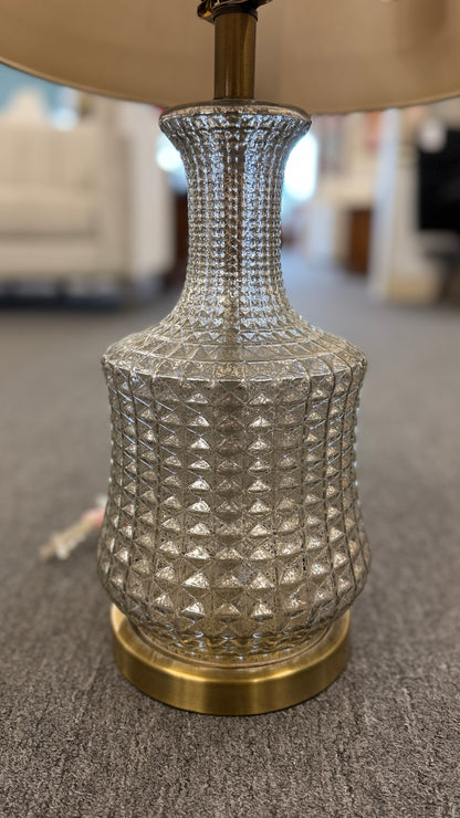 A modern transitional accent lamp featuring a diamond-quilted tinted glass urn base on a brass platform with a beige linen drum shade.