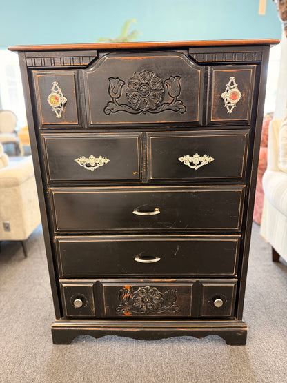 Distressed black wooden five-drawer chest featuring carved floral details, ornate metal drawer hardware, and an antique-inspired finish.