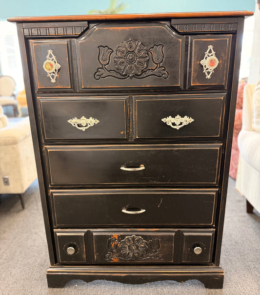 Distressed black wooden five-drawer chest featuring carved floral details, ornate metal drawer hardware, and an antique-inspired finish.